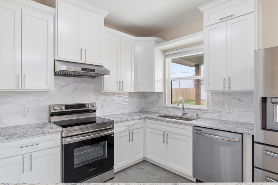 Kitchen featuring stainless steel appliances, white cabinetry, and light stone counters