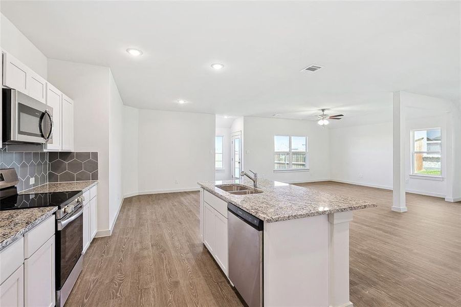 Kitchen with white cabinets, sink, a center island with sink, appliances with stainless steel finishes, and light hardwood / wood-style floors