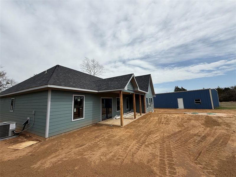 Back of property featuring central air condition unit, an outbuilding, and a shingled roof