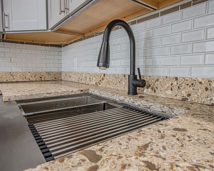 Details with white cabinetry, light stone counters, tasteful backsplash, and a sink