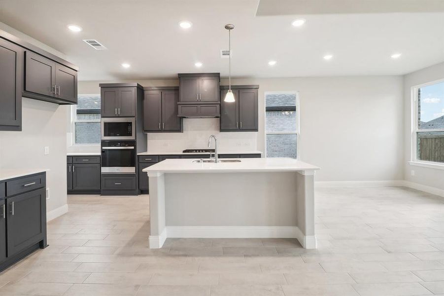 Kitchen with decorative backsplash, appliances with stainless steel finishes, sink, pendant lighting, and a center island with sink