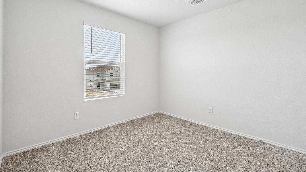 An inviting room features light-colored carpet and a window with blinds, offering neighborhood views.