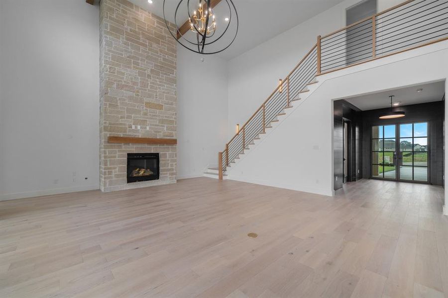 Unfurnished living room with light hardwood / wood-style flooring, an inviting chandelier, a stone fireplace, and a high ceiling