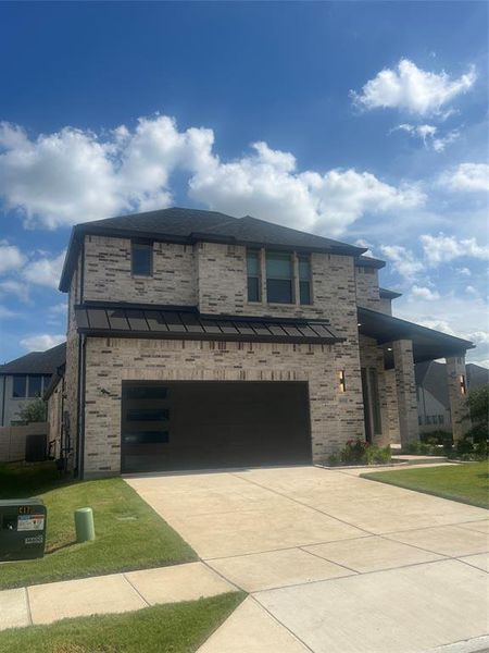 Two-story brick exterior featuring a black roof, modern garage door with frosted panels, covered entry porch, and dual exterior wall sconces Two-story brick exterior featuring a black roof, modern garage door with frosted panels, covered entry porch, and dual exterior wall sconces