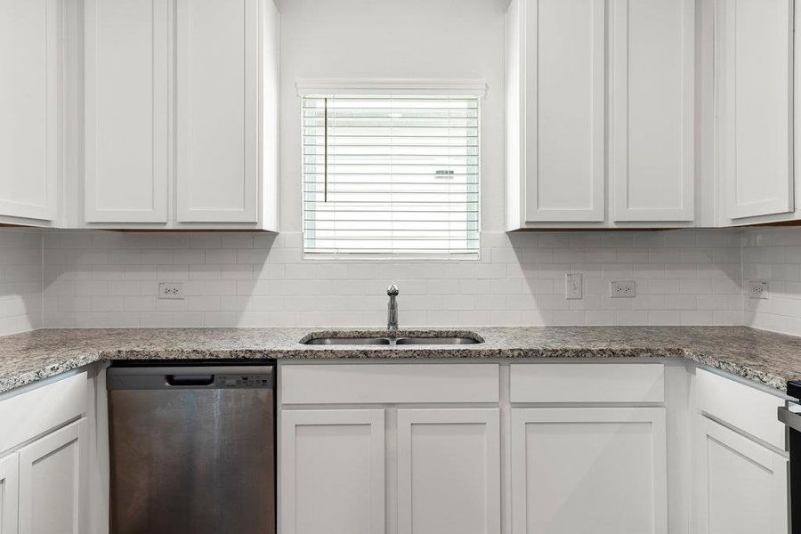 Kitchen featuring dishwasher, light stone counters, white cabinets, and backsplash