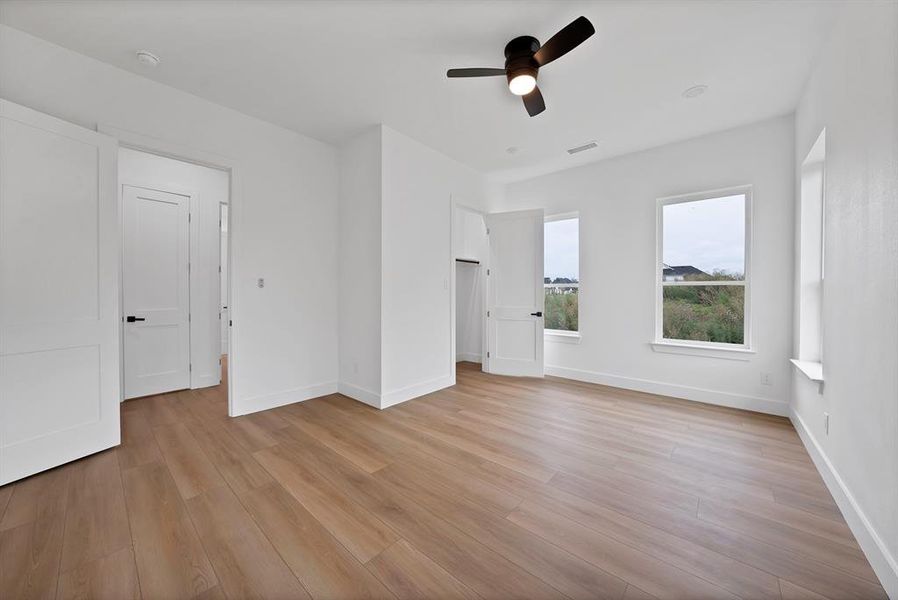 Spacious room featuring wood-finish flooring, white walls, and a ceiling fan with integrated lighting