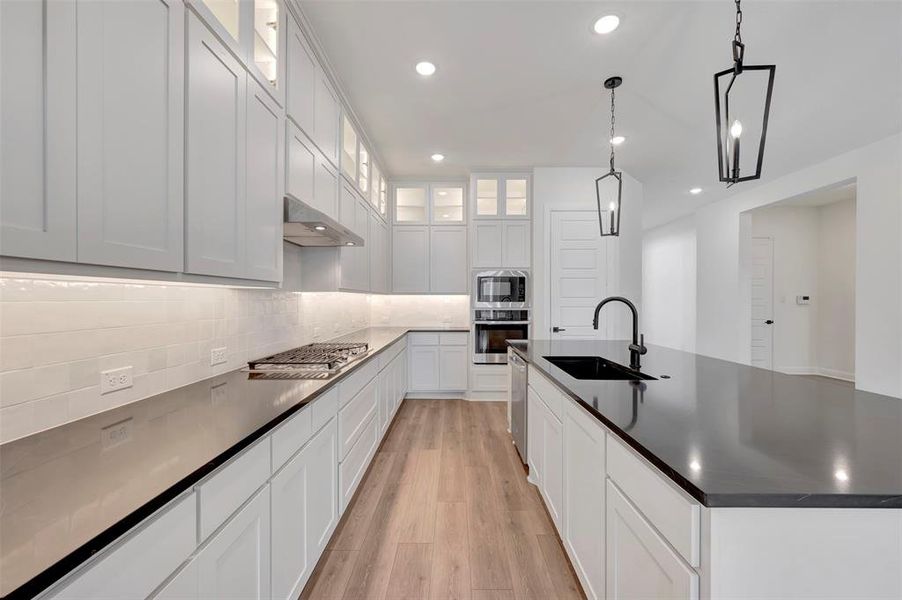 Kitchen with glass fronted cabinets, white cabinetry, light wood-style flooring, and a large island with sink
