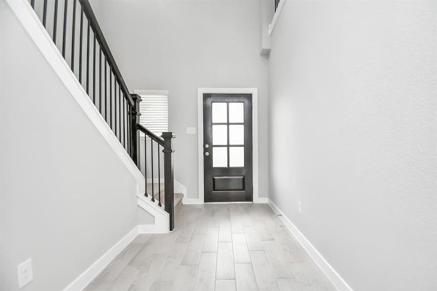 A bright entryway with a wood front door featuring glass panels, a staircase with wooden banisters, and tiled flooring.