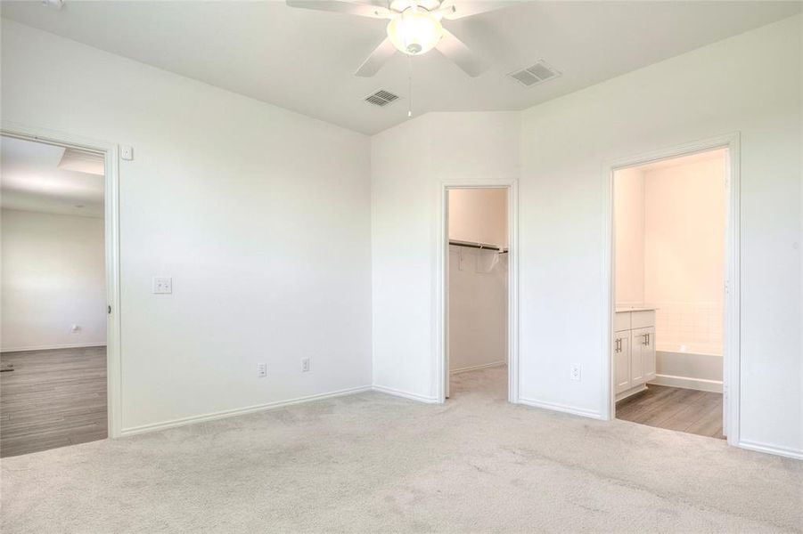 Unfurnished bedroom with a spacious closet, light carpet, a ceiling fan, and ensuite bathroom Unfurnished bedroom with a spacious closet, light carpet, a ceiling fan, and ensuite bathroom