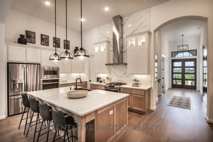 Kitchen featuring stainless steel appliances, wall chimney range hood, a sink, arched walkways, and a towering ceiling Kitchen featuring stainless steel appliances, wall chimney range hood, a sink, arched walkways, and a towering ceiling