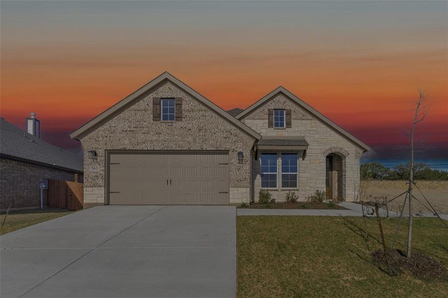 French country inspired facade featuring brick siding, concrete driveway, a yard, and stone siding