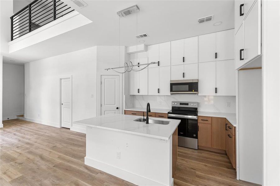 Modern kitchen featuring a large island with an undermount sink, a sleek black faucet, and white quartz countertops