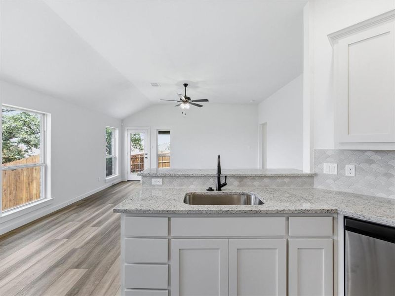 Kitchen island with a stainless steel sink and matte black faucet, granite countertops, white shaker cabinetry, and a scalloped tile backsplash Kitchen island with a stainless steel sink and matte black faucet, granite countertops, white shaker cabinetry, and a scalloped tile backsplash