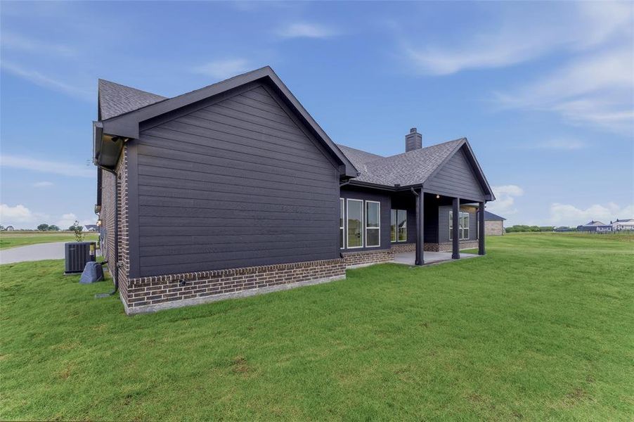 Exterior featuring dark siding with brick wainscoting, an integrated covered patio with columns, a dark shingle roof, and multiple windows Exterior featuring dark siding with brick wainscoting, an integrated covered patio with columns, a dark shingle roof, and multiple windows