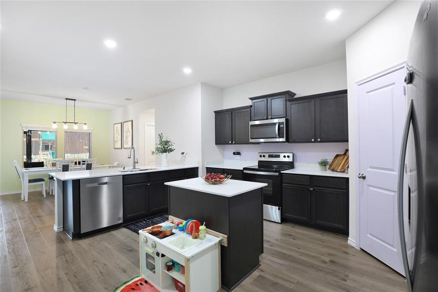 Kitchen with appliances with stainless steel finishes, a kitchen island, decorative light fixtures, light wood-type flooring, and a peninsula
