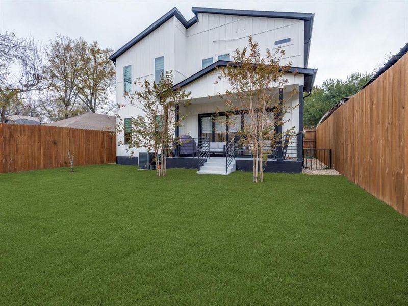 Expansive artificial turf backyard featuring a covered patio, black exterior railings, a privacy fence, and a side gate Expansive artificial turf backyard featuring a covered patio, black exterior railings, a privacy fence, and a side gate