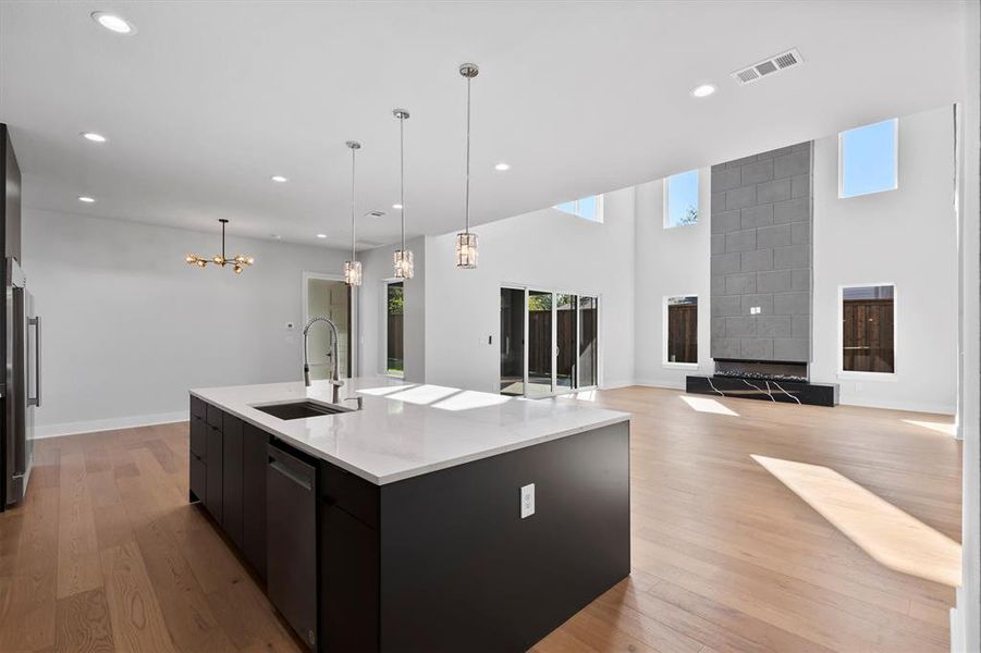 Kitchen with stainless steel dishwasher, sink, a large island with sink, decorative light fixtures, and light hardwood / wood-style flooring