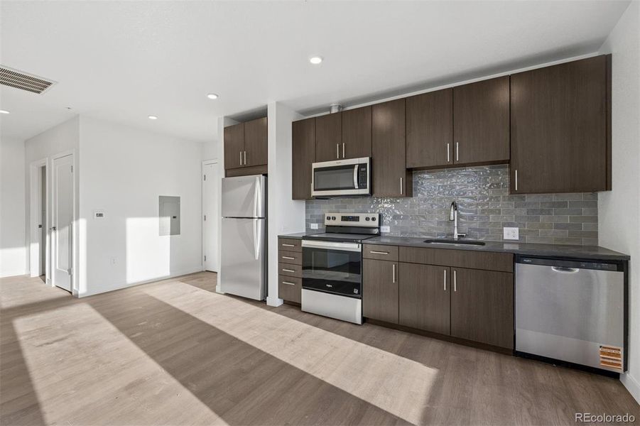 Contemporary kitchen with quartz countertops, stainless steel appliances, tile backsplash, and ample cabinet storage.