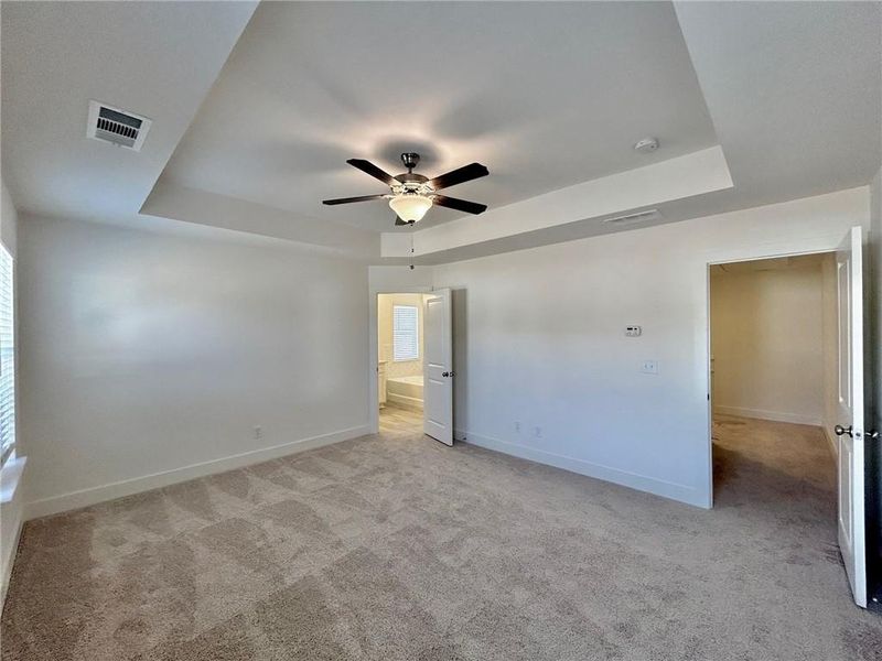 Unfurnished room featuring a tray ceiling, ceiling fan, and light colored carpet