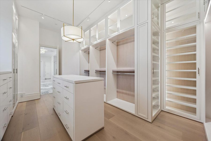1/2 primary closets, this expansive wardrobe offers custom built-ins with ample hanging space, generous shelving, dedicated shoe storage, sleek drawers and glass doors. A beautiful light fixture above the center island adds both function and elegance.