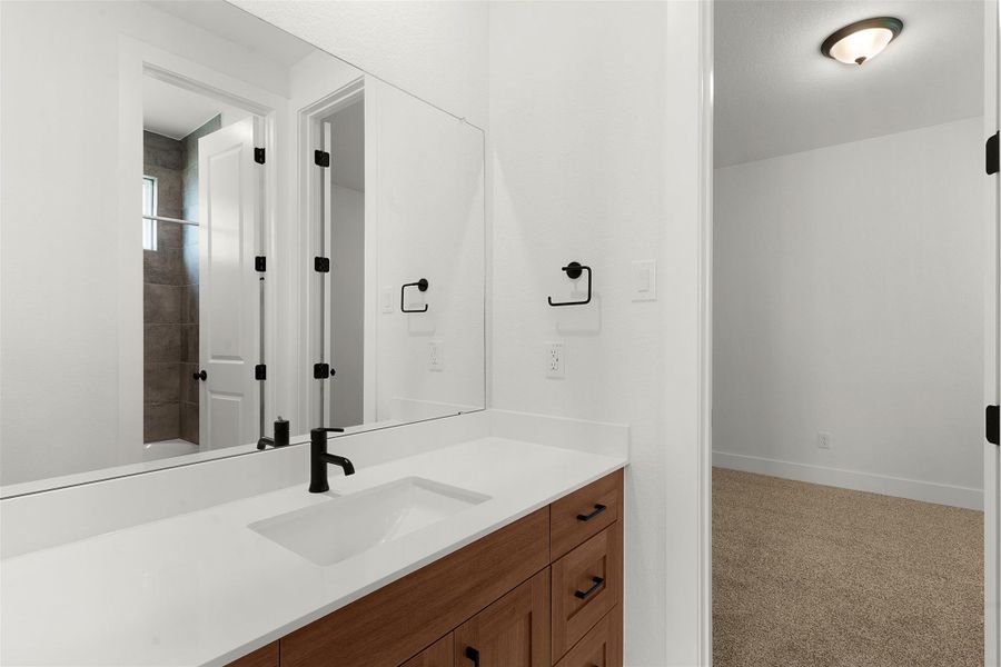 Bathroom featuring a wood-finish vanity with a white countertop and integrated sink Bathroom featuring a wood-finish vanity with a white countertop and integrated sink