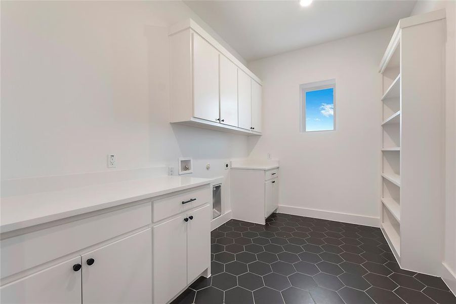 Clothes washing area with hookup for a washing machine, dark tile patterned flooring, and cabinets