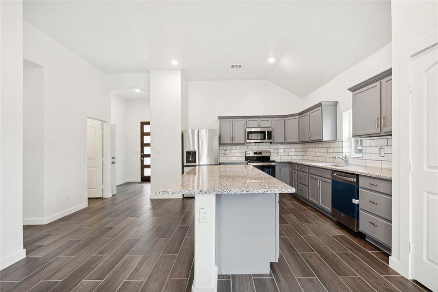 Kitchen featuring gray cabinetry, appliances with stainless steel finishes, a center island, dark wood-type flooring, and light stone counters