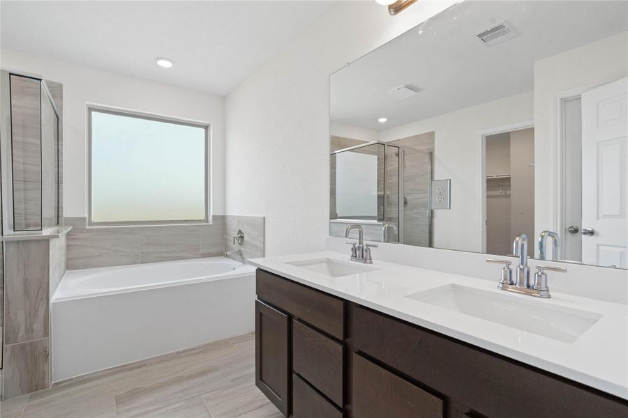 This beautiful primary bathroom is move-in ready! It showcases stained cabinetry paired with light countertops, dual vanity sinks, a large mirror, a spacious walk-in closet with built-in shelving, high ceilings, custom paint, and stylish modern finishes throughout.