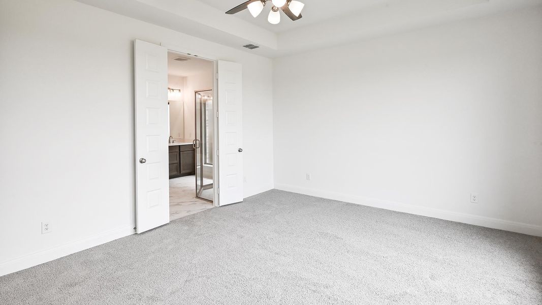Unfurnished bedroom with light colored carpet, baseboards, ensuite bath, and ceiling fan