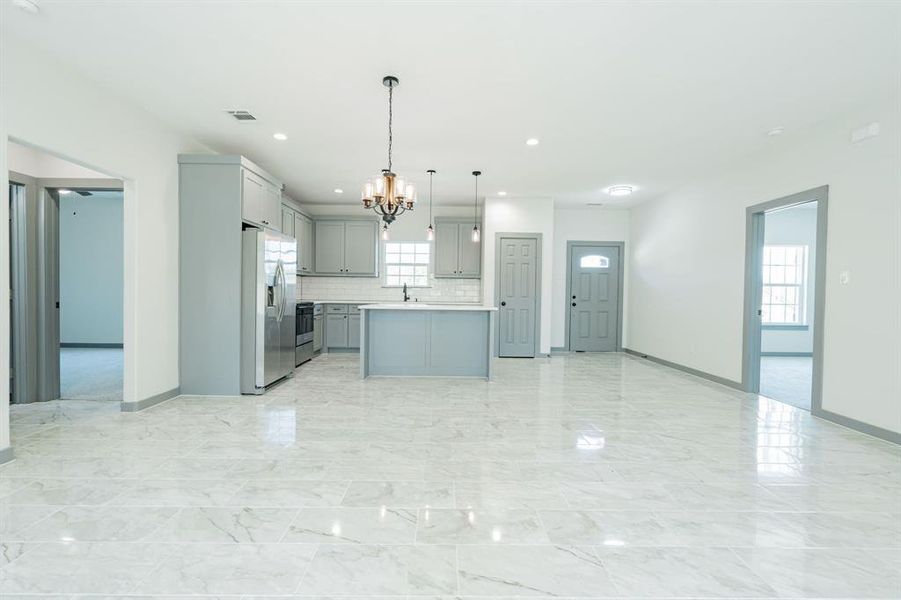 Kitchen featuring decorative backsplash, a chandelier, stainless steel refrigerator with ice dispenser, a kitchen island, and light tile patterned floors