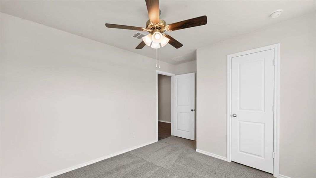 Carpeted room featuring a ceiling fan with light fixture, light gray walls, white trim, and two white two-panel doors Carpeted room featuring a ceiling fan with light fixture, light gray walls, white trim, and two white two-panel doors