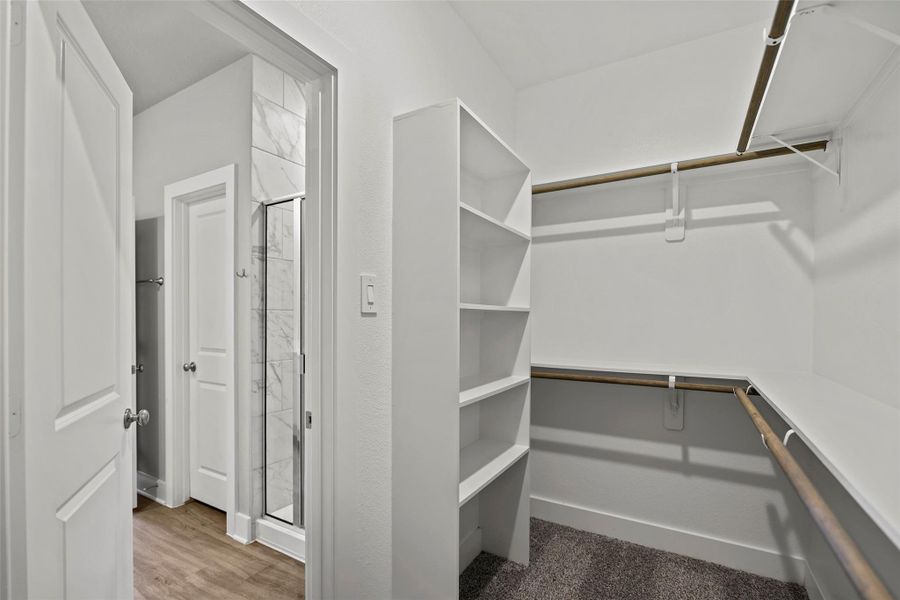 Large walk-in closet in primary bedroom with built in shelves and hanging rods.