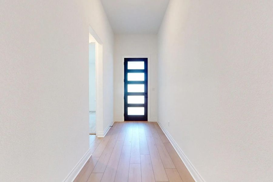 Entryway featuring light-toned hardwood flooring, white baseboards, and a dark modern door with five frosted glass panels