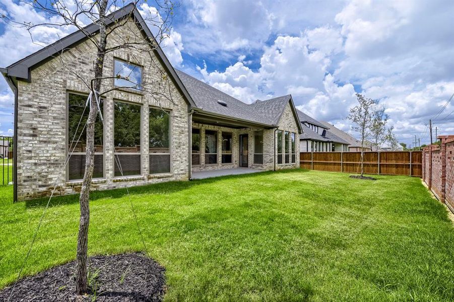 Expansive backyard featuring a manicured lawn, a full brick exterior, a covered patio, and large windows Expansive backyard featuring a manicured lawn, a full brick exterior, a covered patio, and large windows
