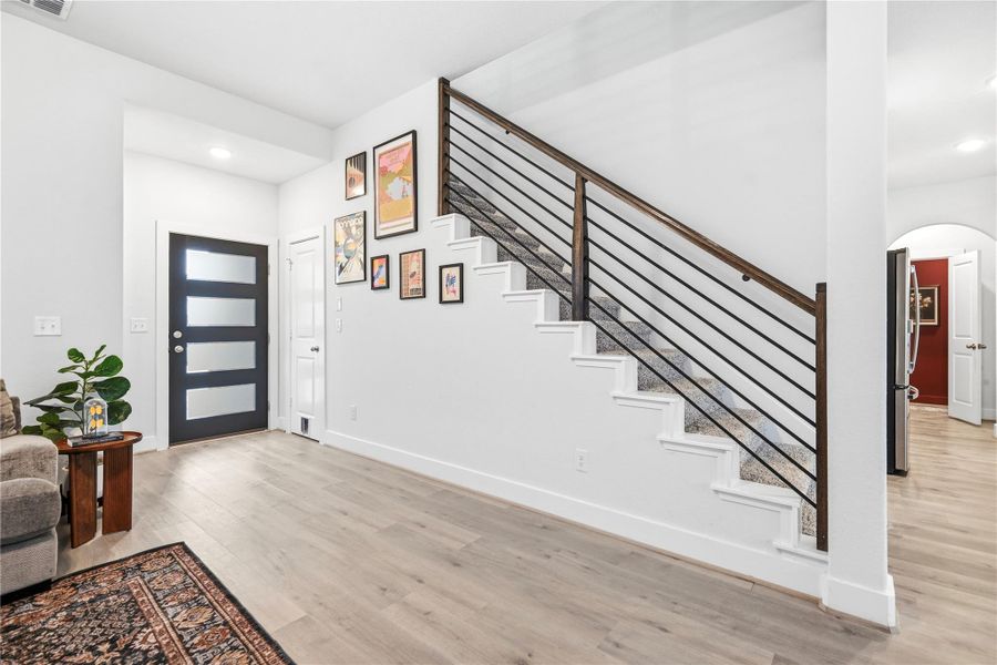 A modern staircase with sleek black railings leads to the upper level, complementing the light wood flooring.
