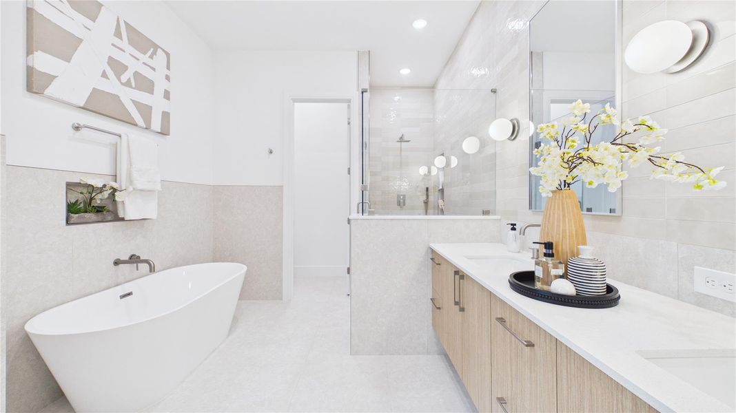 This bathroom features a modern design with a freestanding tub, spacious walk-in shower, and a double vanity. It has sleek, light-colored tiles, ample lighting, and elegant decor accents, creating a bright and luxurious atmosphere.
