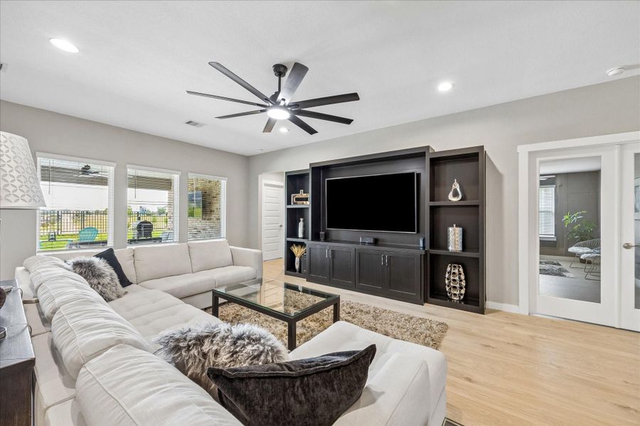 Great view of the living room, with the private office to the right through the French doors.  The custom built-in entertainment center.  The door to the left of the entertainment center leads to the primary retreat with en suite bathroom.  The wall of windows look out to your covered back patio with ceiling fan and outlet for a TV.