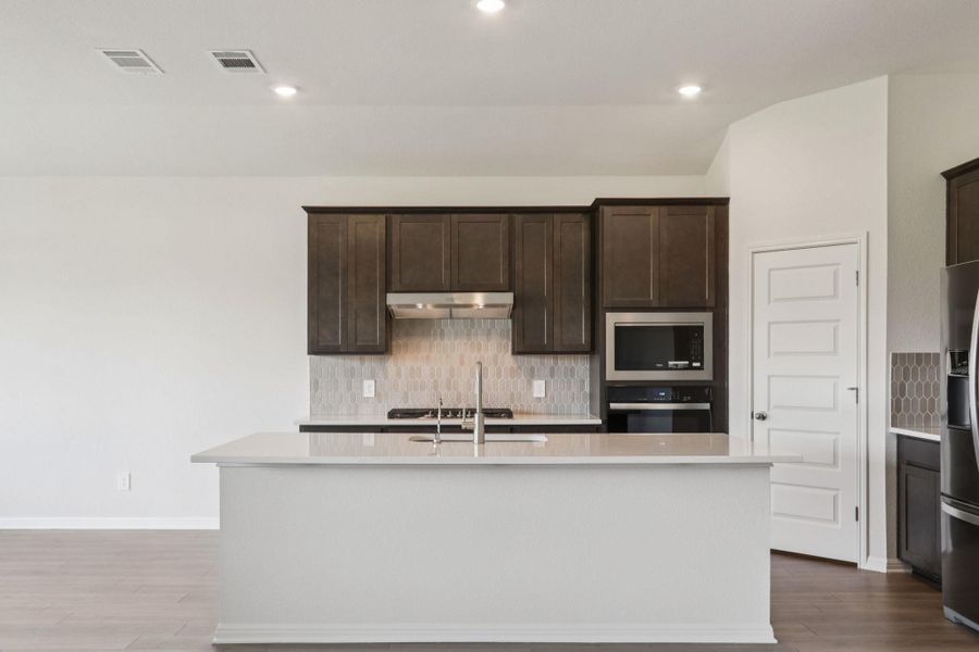 Kitchen featuring decorative backsplash, dark brown cabinets, dark wood-style flooring, light stone counters, and recessed lighting Kitchen featuring decorative backsplash, dark brown cabinets, dark wood-style flooring, light stone counters, and recessed lighting