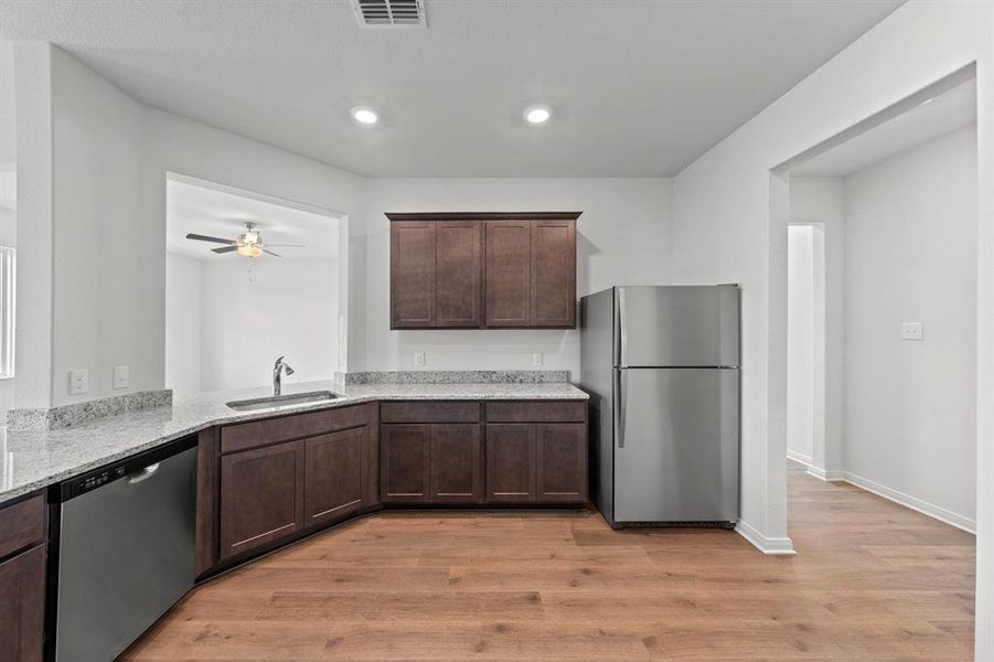 Kitchen featuring stainless steel appliances, dark brown cabinets, light stone countertops, light wood-style flooring, and recessed lighting Kitchen featuring stainless steel appliances, dark brown cabinets, light stone countertops, light wood-style flooring, and recessed lighting