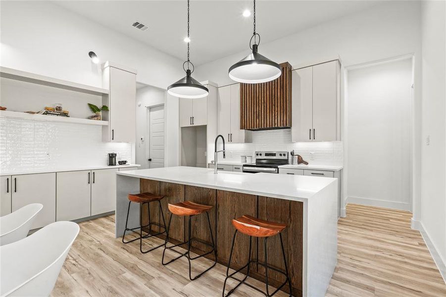 Kitchen with backsplash, light stone countertops, light wood-type flooring, a kitchen island with sink, and a breakfast bar