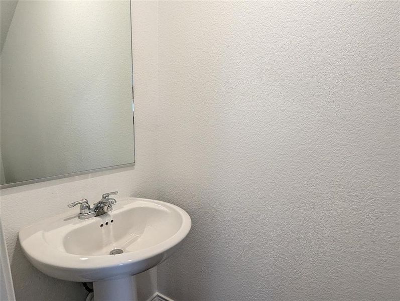 A pristine pedestal sink paired with a simple wall-mounted mirror offers functionality in this compact space.