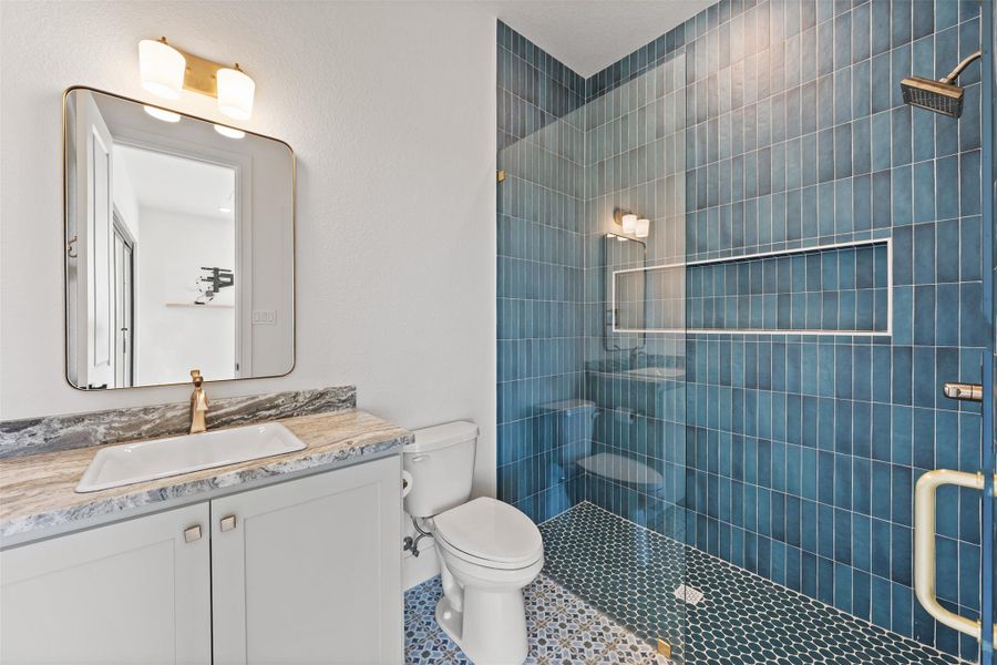 Bathroom featuring vanity, tile patterned floors, toilet, and tiled shower