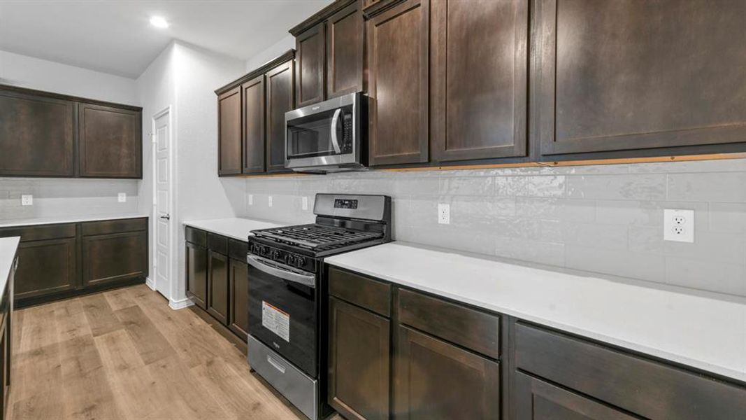 Kitchen with stainless steel appliances, dark wood finish cabinetry, light wood-style flooring, recessed lighting, and tasteful backsplash Kitchen with stainless steel appliances, dark wood finish cabinetry, light wood-style flooring, recessed lighting, and tasteful backsplash