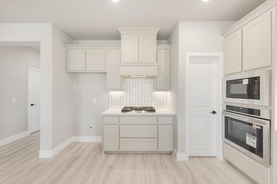 White kitchen with gas cooktop, built-in oven and microwave, tile backsplash, and light wood floors