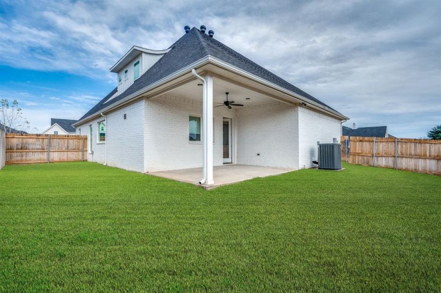 Rear view of house with central air condition unit, ceiling fan, a patio area, and a lawn