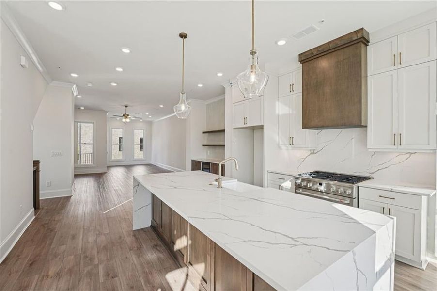 Kitchen featuring wood finished floors, crown molding, white cabinets, backsplash, and light stone countertops Kitchen featuring wood finished floors, crown molding, white cabinets, backsplash, and light stone countertops