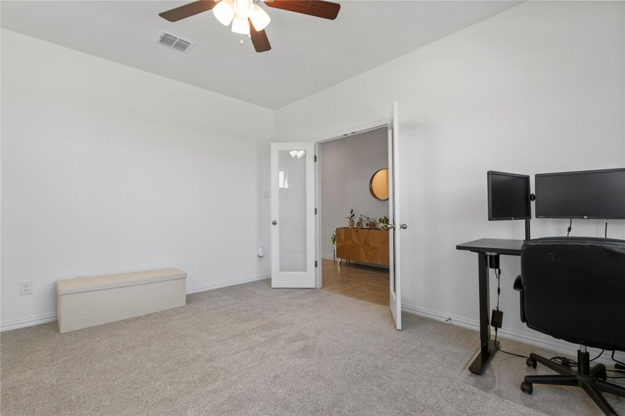 A versatile home office features plush carpeting and French doors, offering a quiet workspace. A versatile home office features plush carpeting and French doors, offering a quiet workspace.