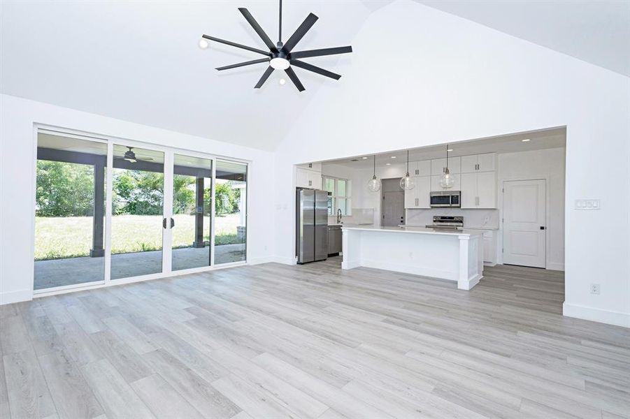 Unfurnished living room with a ceiling fan, high vaulted ceiling, and light wood finished floors