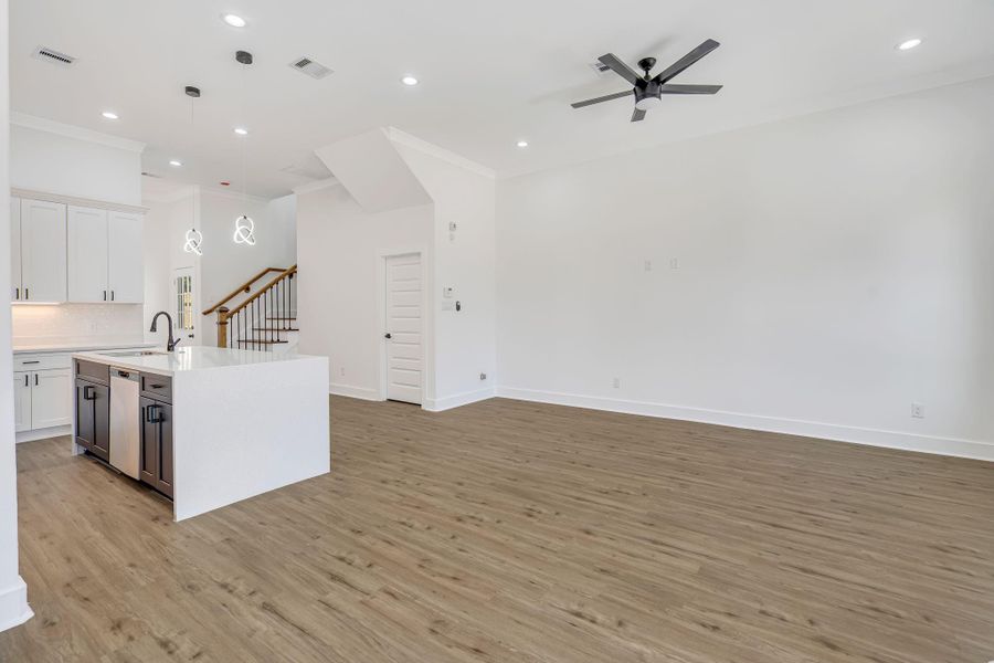 Spacious open-concept living and kitchen area featuring over 10-ft ceilings, commercial-grade LVP flooring, recessed LED lighting, and a large waterfall quartz island with modern pendant lighting.