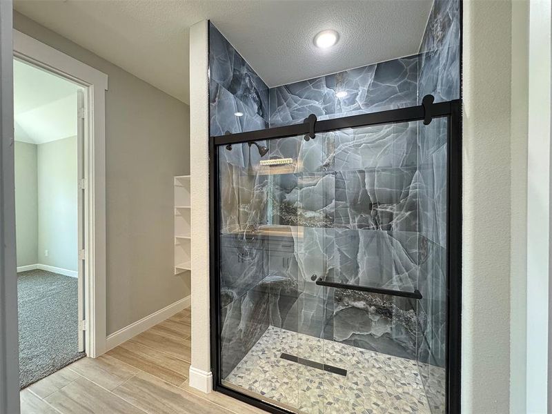 Walk-in shower featuring a dark-toned patterned tile surround, clear glass enclosure with matte black hardware, and a pebble-style tile floor